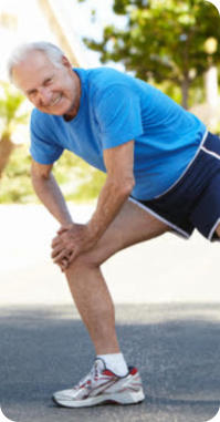 Photo of a senior man in running clothes on an outdoor path doing a lunging stretch.